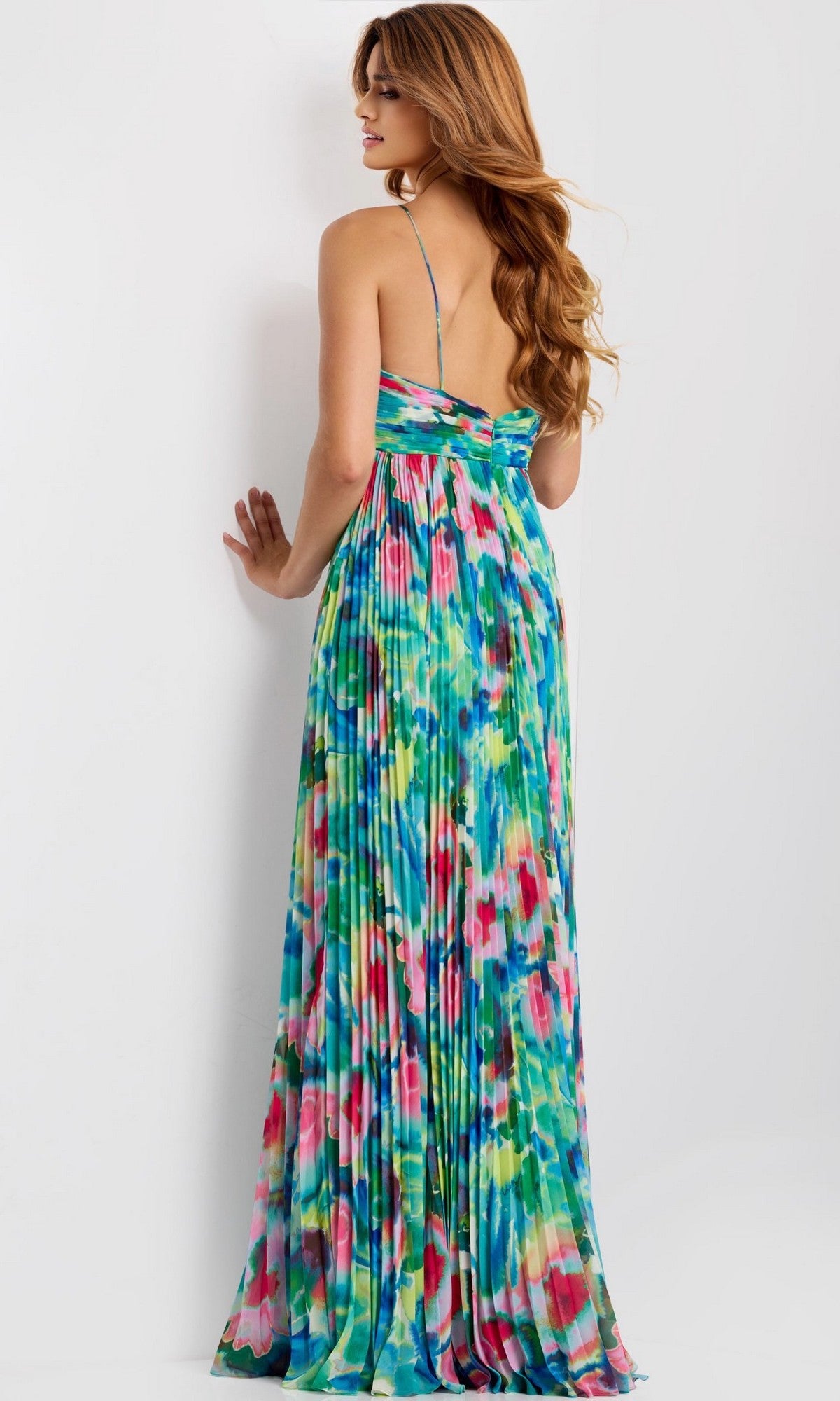 A woman with long, wavy hair models the Jovani 42558 Long Prom Dress—a floor-length, strappy gown with a colorful abstract floral print—photographed from the back against a plain light background.